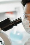 Scientist wearing protective glasses and a face mask while observing through a microscope in a laboratory